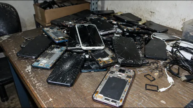 Pilha de celulares com telas quebradas sobre mesa riscada